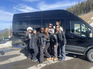 Smiling group standing beside a black passenger van in the Colorado mountains
