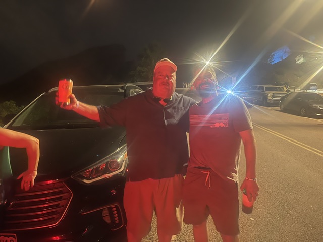Two passengers standing beside a black vehicle at night
